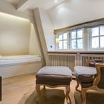 Zimmer mit Bett, Sessel und Fenster. Holzboden und Fernseher.