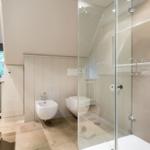 Badezimmer mit Dusche, Toilette und Bidet. Holzwand und Steinboden.