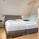 Schlafzimmer mit Doppelbett, Holzboden und schräger Decke mit Balken.