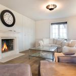 Wohnzimmer mit Kamin, Sofa und Glas-Tisch. Wanduhr und Fenster sichtbar.
