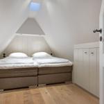 Schlafzimmer mit Doppelbett, Holzboden und Dachschrägen. Weiße Schränke und Dachfenster.