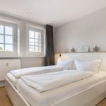 Bedroom with white bed, two windows, and wooden floor.