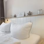 Bedroom with white bed, wood panels, and wall lighting.