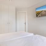 Bedroom with white bed, wardrobe, and wall picture of a beach.