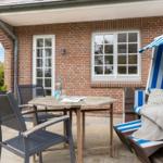 Terrace with table, chairs, and beach chair in front of brick house