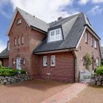 Red brick house with gray roof and paved yard.