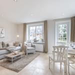 Living and dining area with sofa, armchair, table and chairs. Windows with curtains and view of garden.