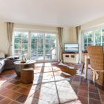 Wohn- und Essbereich mit Terrassentür, TV und Wickerstühlen auf Terrakottboden.