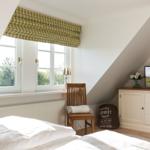 Schlafzimmer mit Dachschräge, Fenster, Bett, Stuhl und TV-Schrank.