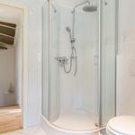 Dusche mit Glaswand, Toilette und Blick in Wohnbereich mit Treppe.