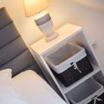 Schlafzimmer mit grauem Kopfteil, weißem Nachttisch und Lampe.