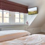 Schlafzimmer mit Dachschrägen, Fenster und TV. Bett mit weißer Bettwäsche.