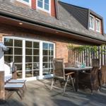 Terrasse mit Tisch, Stühlen und Strandkorb. Hintergrund: Holzzaun und Haus mit Fenstern.