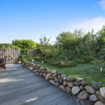 Holzterrasse mit Garten, Steinmauer und Sitzgelegenheiten.