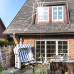 Terrasse mit Strandkorb, Tisch und Stühlen vor einem Haus mit Schiebetüren und Dachfenstern.