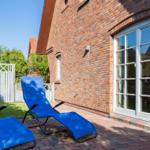 Zwei blaue Liegestühle auf Terrasse neben Backsteinhaus mit Fenster.