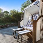 Hochwertiger Strandkorb mit blau-weißem Polster und Holzgestell auf Holzterrasse.