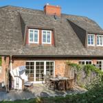 Haus mit Terrasse, Garten und Dachfenstern. Einrichtung für Außensitzgelegenheit.