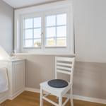 Bedroom with white bed, chair, and window. Wooden floor and two-tone walls.