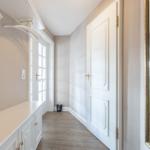 Hallway with coat rack, door, and mirror. Wooden floor and white doors.