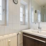 Bathroom with sink, mirror, and window. Shower in the background.