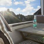 Terrace with table, chairs, and water bottle. View of rooftops and hills under blue sky.