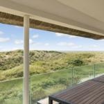 Terrasse mit Blick auf Dünen und Meer unter strohgedecktem Dach.