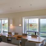 Esszimmer mit Tisch, Stühlen und Blick auf Grasland und Meer.