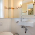 Badezimmer mit Waschbecken, Spiegel und Fenster. Wandverkleidung und Muscheldekor.