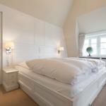 Schlafzimmer mit weißem Bett, Nachttisch und Fenster