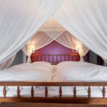 Hochbetten mit weißer Bettwäsche und weißen Vorhängen. Hinter dem Bett steht eine rosa Wand.