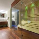 Sauna mit Holzbänken und Glaswand. Neben dem Bad mit Dusche und Waschbecken.