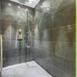 Dusche mit grauen Fliesen und grüner Mosaikwand