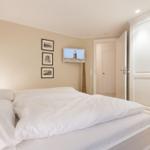 Schlafzimmer mit weißem Bett, Kleiderschrank und Wandbildern.
