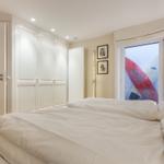 Schlafzimmer mit weißem Bett, Schwebetüren und Fenster mit Surfbrettern.