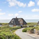 Haus mit Strohdach am Meer, gepflasterter Weg und Blumenbeete.