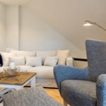 Wohnzimmer mit Sofa, Sessel und Tisch unter schrägen Wänden.