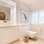 Badezimmer mit Waschbecken, Toilette und Spiegel. Fenster mit Jalousien und Wandbild.