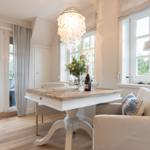 Esszimmer mit Holztisch, Stühlen und Fenstern. Deckenleuchte und Blumen auf Tisch.