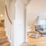 Helle Treppe führt in ein Wohnzimmer mit Sitzmöbeln und Fenster.