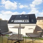 Terrace with two chairs, table, and Buddha statue. View of rooftops and sky.