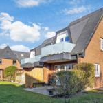 Red brick building with balcony and garden under blue sky.