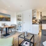 Living kitchen with dining table, sofa, and kitchen cabinets. Wooden floor and wall picture.