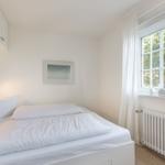 Schlafzimmer mit weißem Bett, Fenster und Heizkörper.