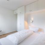 Schlafzimmer mit weißem Bett, Schrank und Stuhl.