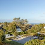 Weitläufiger Blick auf Wohnhäuser, Bäume und Meer unter blauem Himmel.