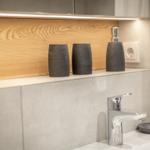 Waschbecken mit modernem Wasserhahn und grauen Accessoires auf Holz- und Steinuntergrund.