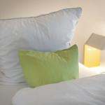 Bettkopf mit weißen und grünen Kissen, daneben eine Lampe.