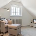 Ein Schlafzimmer mit Sessel, Fußhocker, Fernseher und Fenster unter Dachschräge.