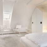 Schlafzimmer mit Dachschrägen, weißem Bett, Stühlen und Fenster.